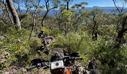 Motorcycle on a rocky trail with a scenic background of trees and mountains.